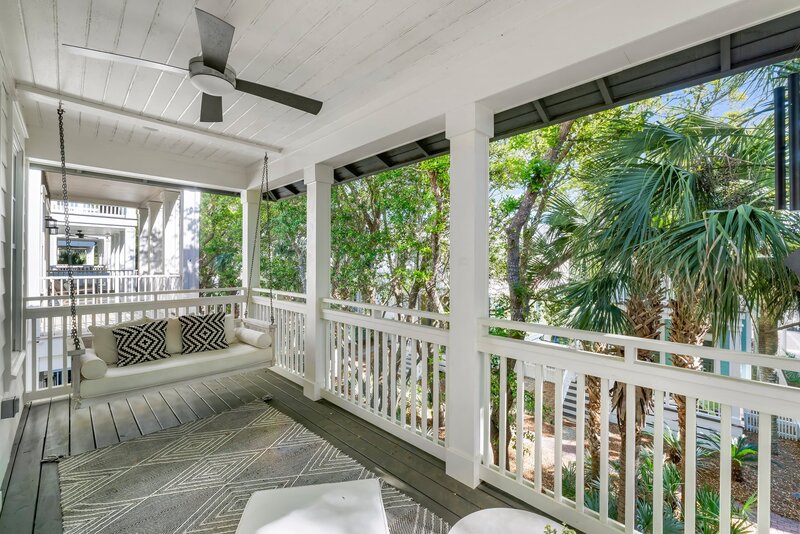 Relaxing porch with white swing, modern rug, and palm tree-lined view at Panama City Beach home