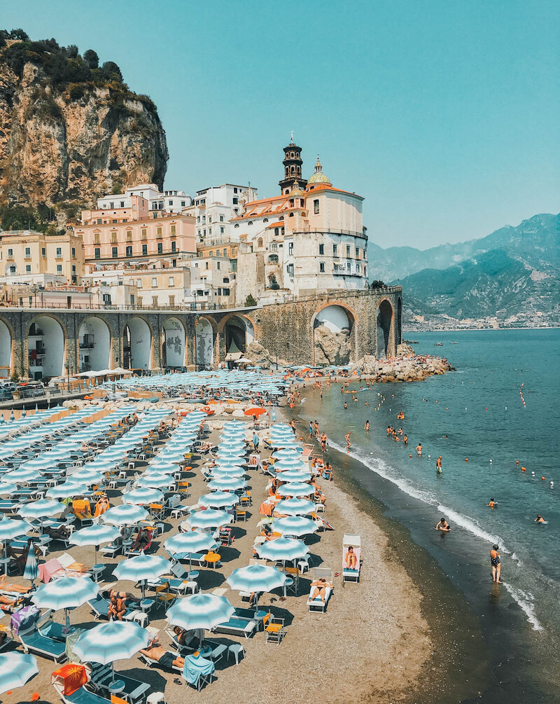 Rows of colorful blue and white beach umbrellas and beach chairs on the sand in Cinque Terre, Italy