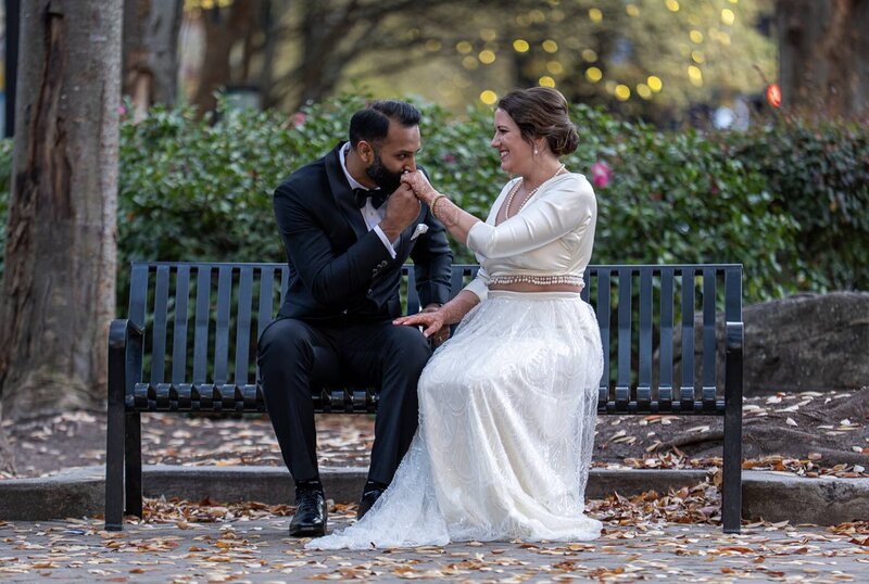 A couple sitting on a bench while one kisses the other's hand