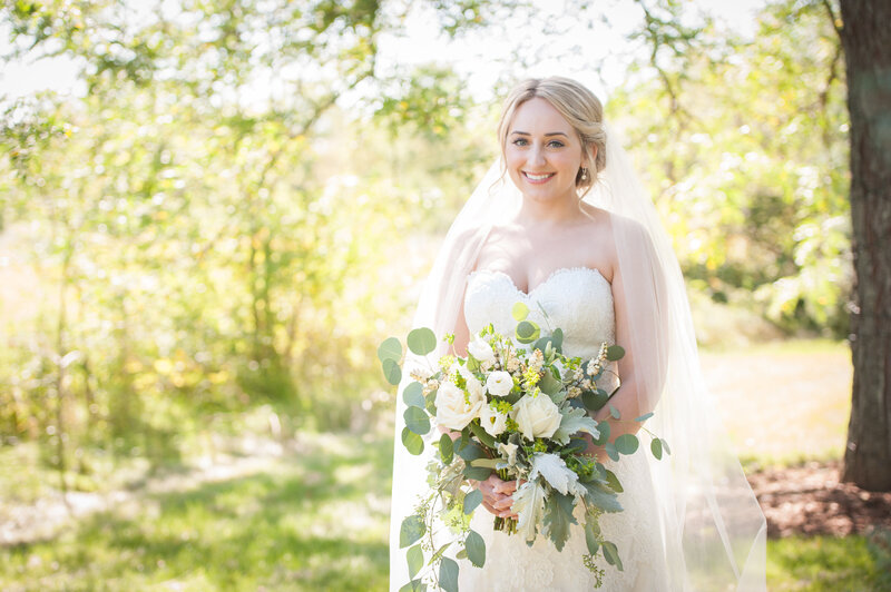 bride smiles at the camera while holding a big green and white bridal bouquet
