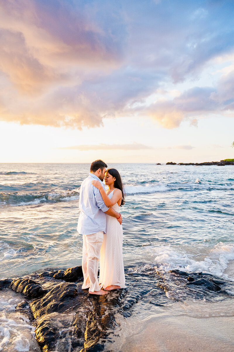 woman and man couple huggin on the beach a t sunset with waves crashing around them