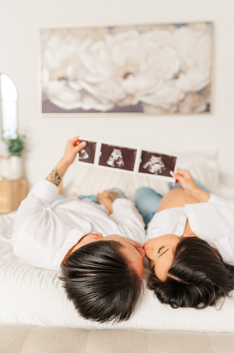 A couple laying on a bed showing their ultrasound as a pregnancy announcement at a maternity session in Lewiston, Idaho