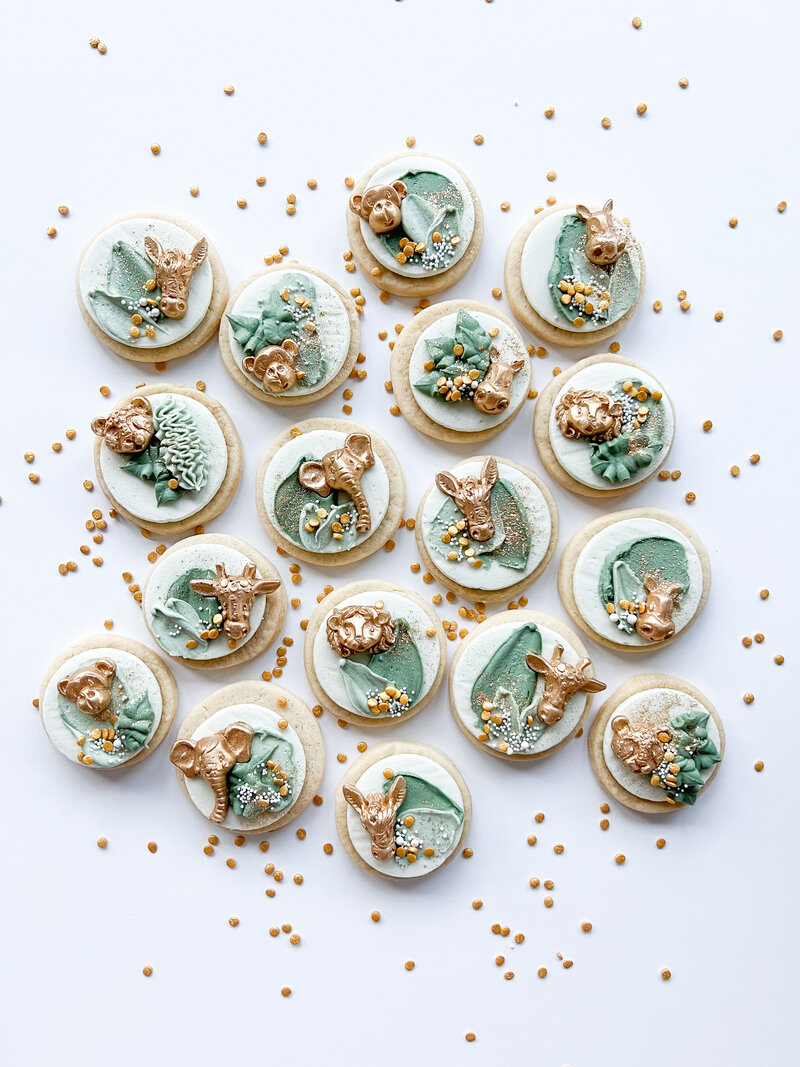 Buttercream cookies frosted with white and green frosting. Gold animal shapes and sprinkles are placed on topl