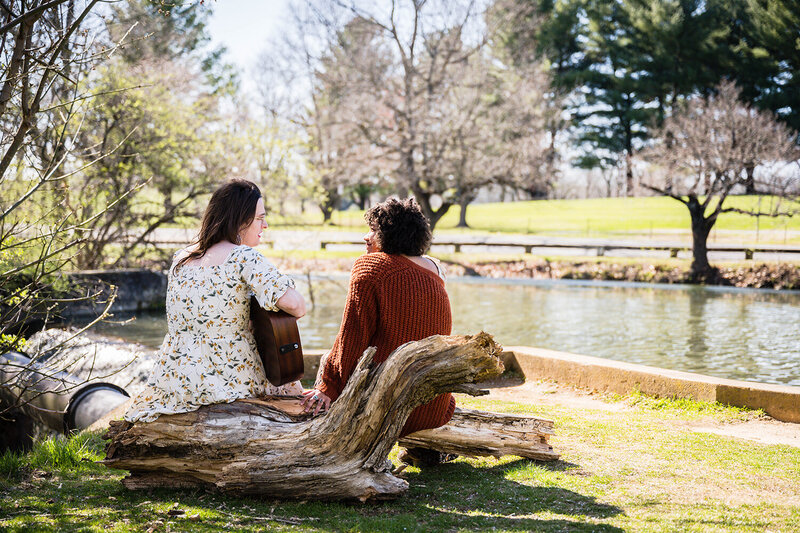 An LGBTQ+ couple sit on a large tree overlooking Duck Pond on their wedding day in Blacksburg.
