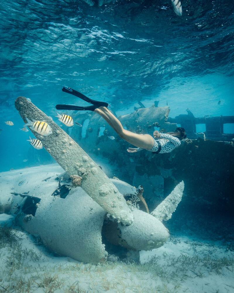 Woman wearing flippers swimming underwater next to a plane propeller