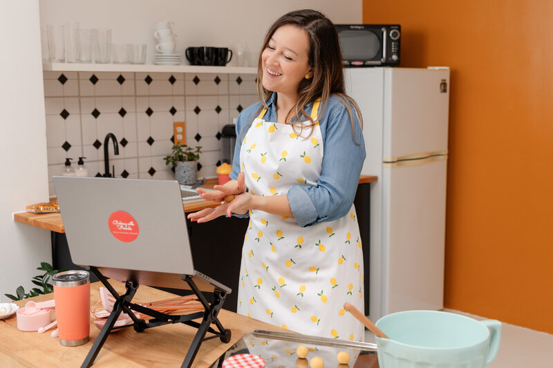 a woman smiles at her laptop while baking cookies
