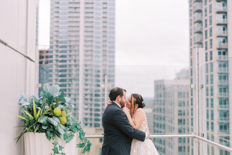 a bride and groom kiss on a rooftop terrace in uptown charlotte