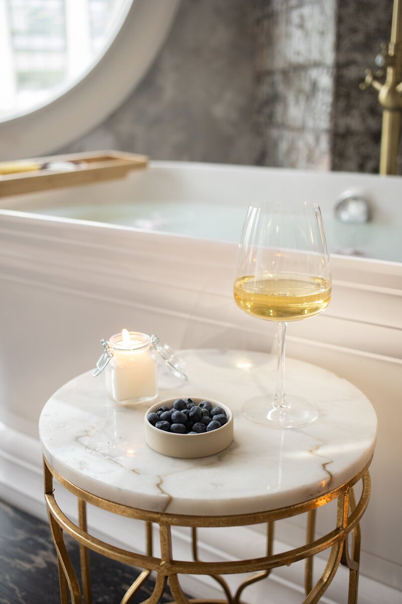Glass of champagne, candle, and berries sitting on table next to bath tub