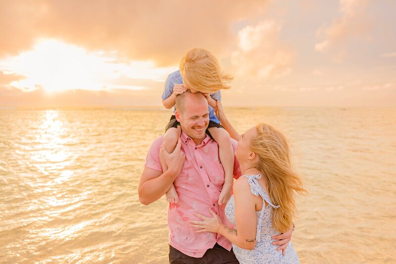 beautiful family portrait with mom pregnant and young boy sitting on dad's shoulders kissing his head in lahaina
