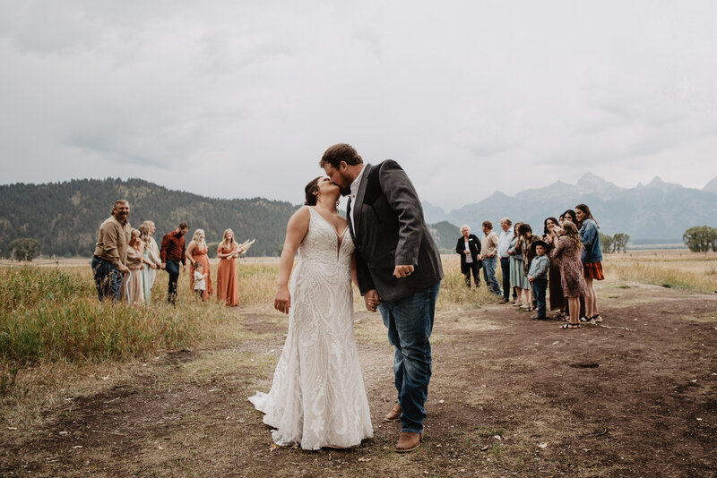 bride adn groom exiting their jackson hole wedding while holding hands and kissing while their friends and family cheer for them in the distance captured by jackson hole wedding  photographers