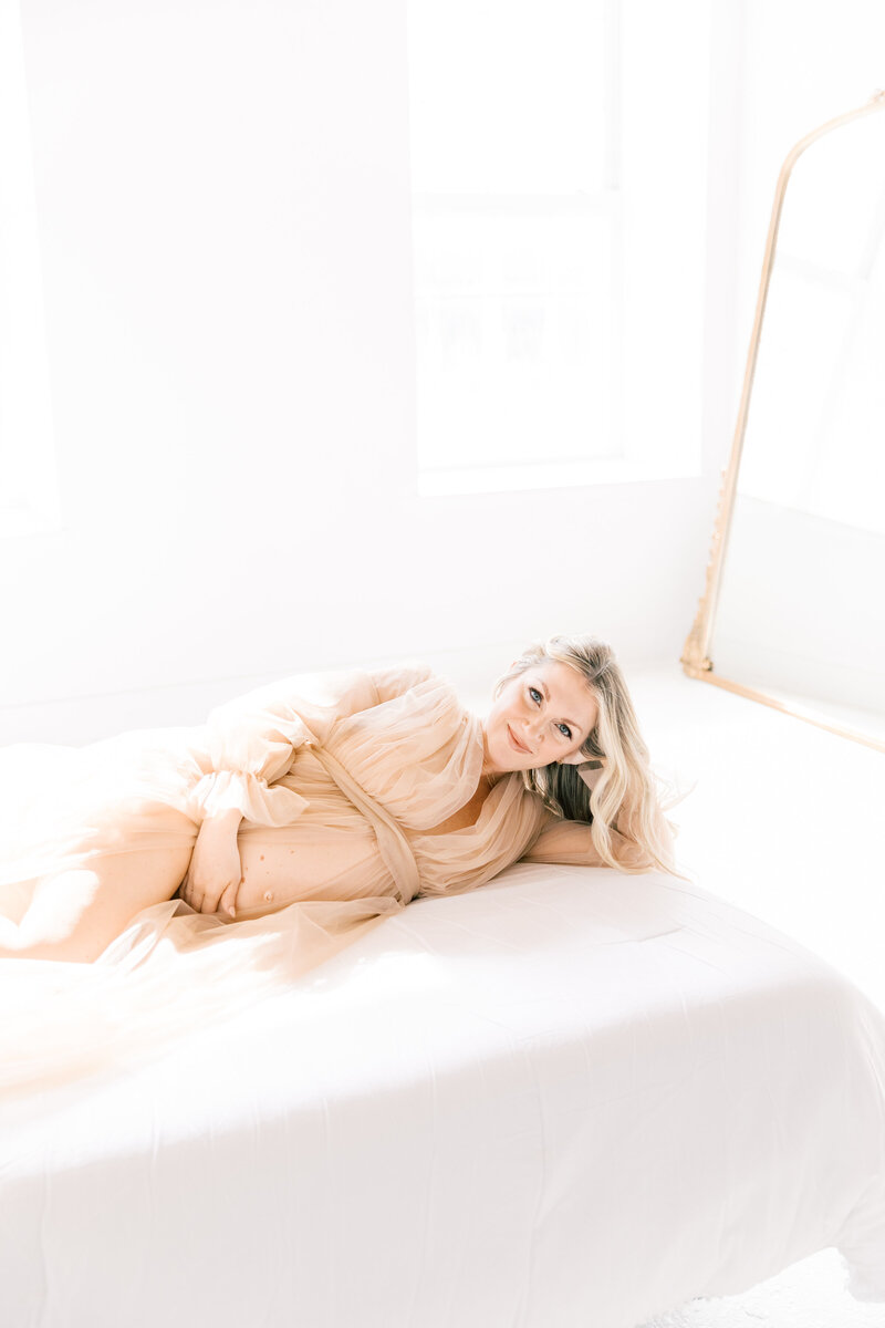 A Charlotte Maternity Photographer image of a blonde woman laying on her side on a bed