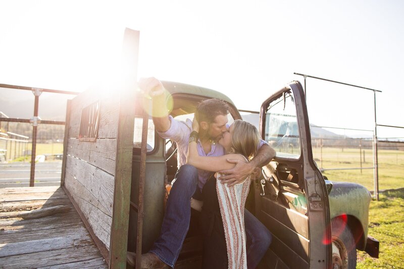 Engaged couple kissing in vintage truck on ranch