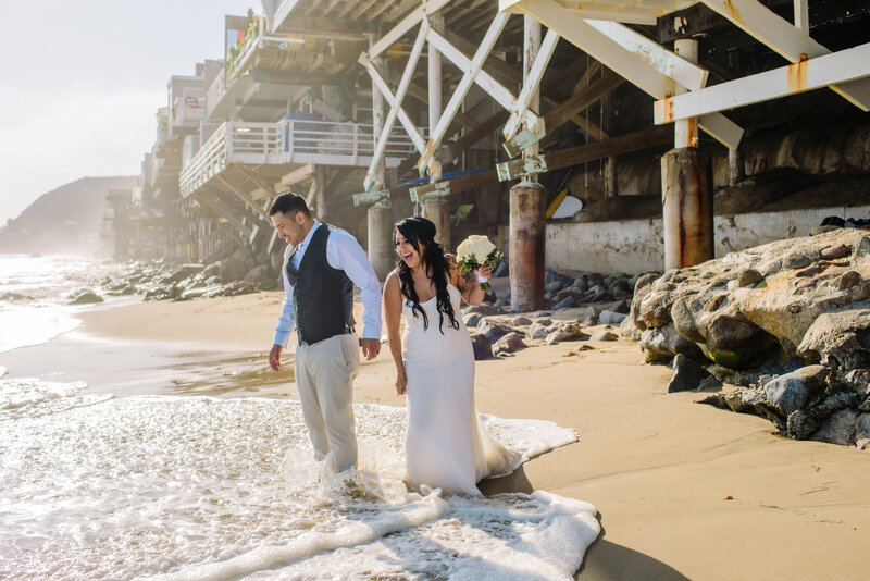 ocean wave splashes up on bride and groom's feet on the beach