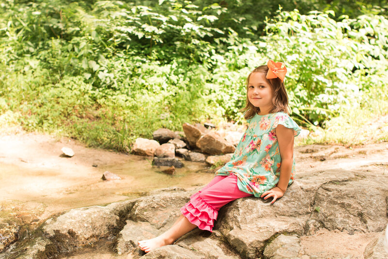 little girl sitting on a rock near a creek
