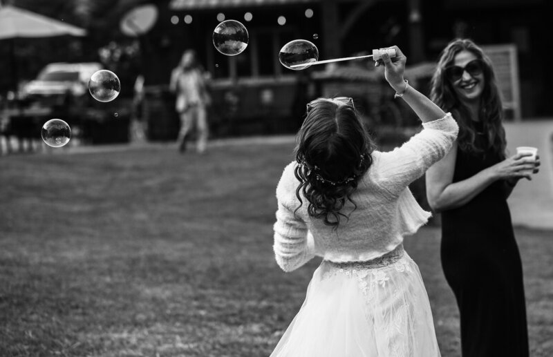 Bride leans back to blow through a bubble wand during Pine Junction wedding reception in Sherman NY
