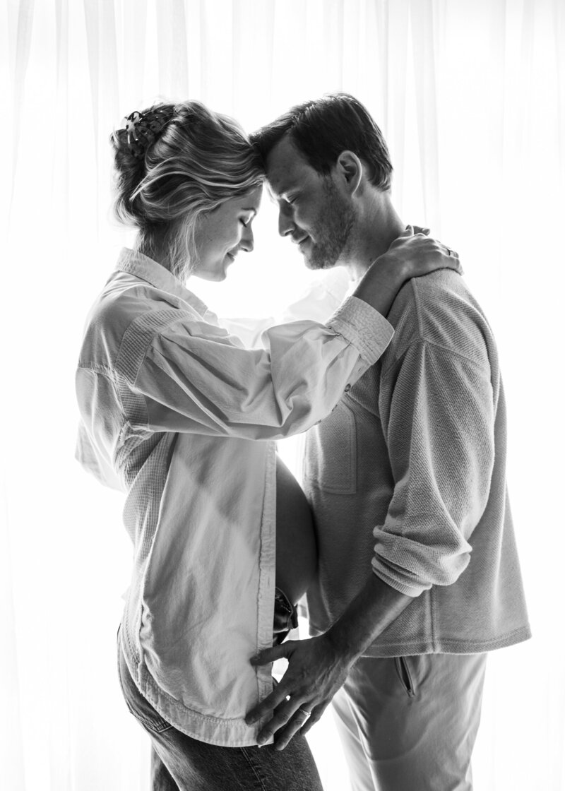 Husband and wife embrace while showing off her pregnant belly.