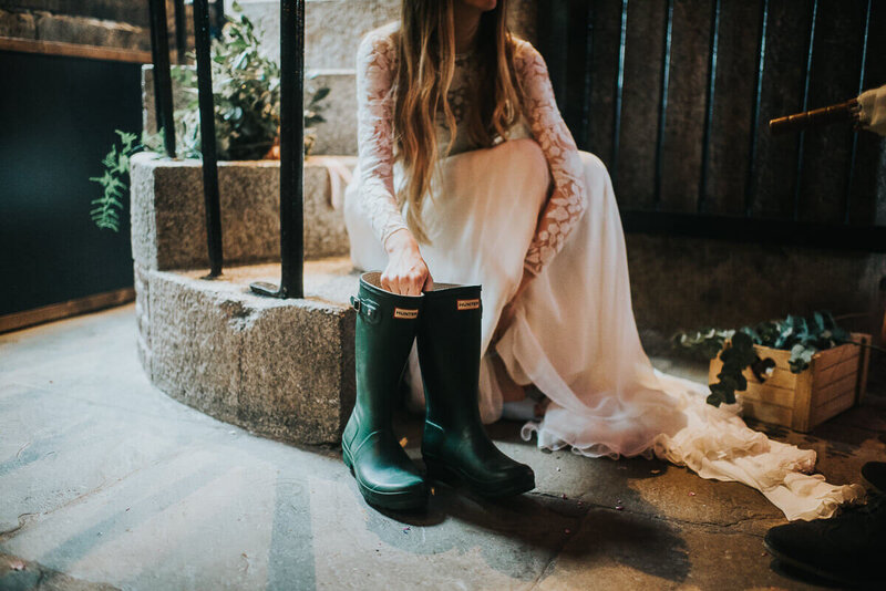 A bride sitting on the steps inside Polhawn Fort about to put in wellies