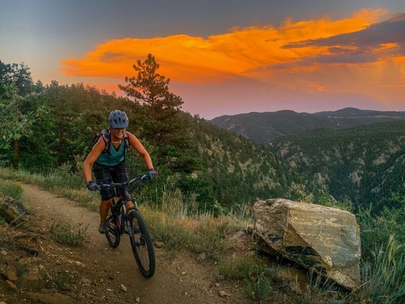 Alison Reuter of A/Revelation designs is mountain biking with a sunset behind