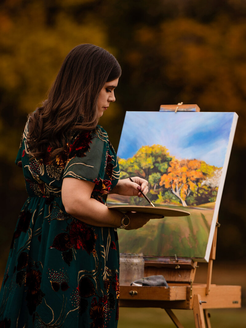 A headshot photo of Debbie smiling at the camera and holding paintbrushes