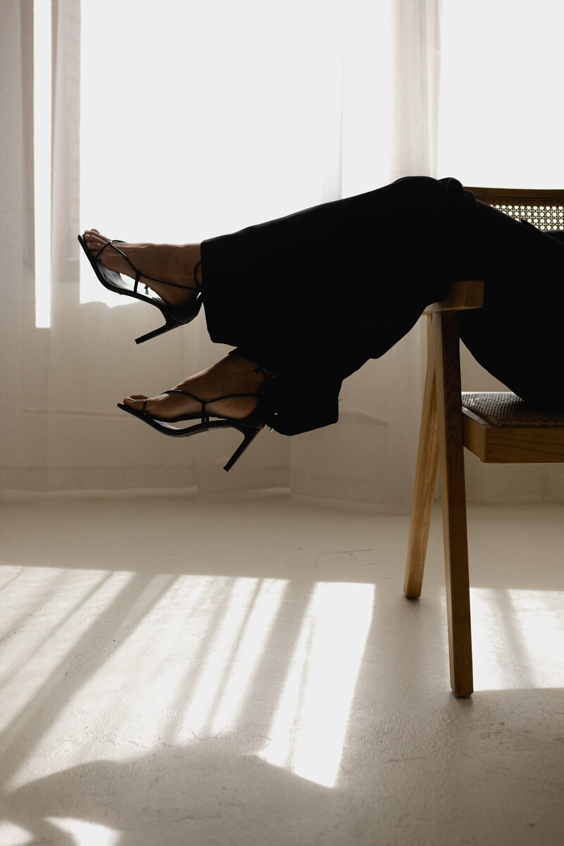 Woman with legs hanging over side of chair in black pants and strappy heels