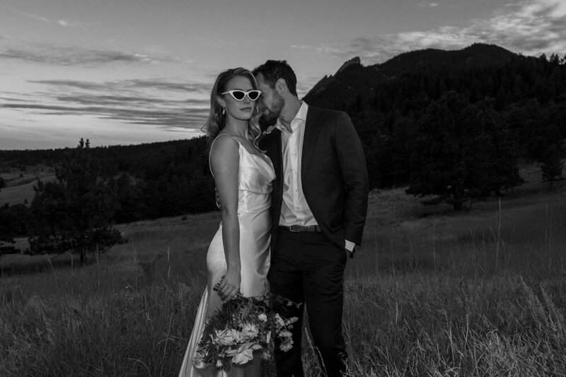 bride and groom in black and white standing in field at boulder wedding