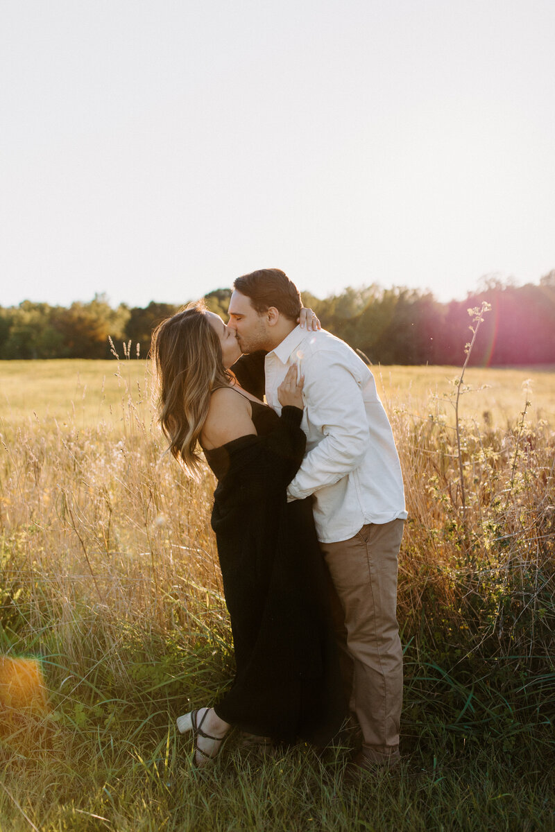 couple standing in a field kissing at sunset