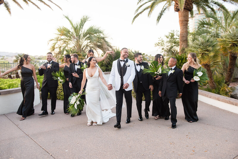 Bridal party in black and white attire posing with the couple in the lush courtyard.