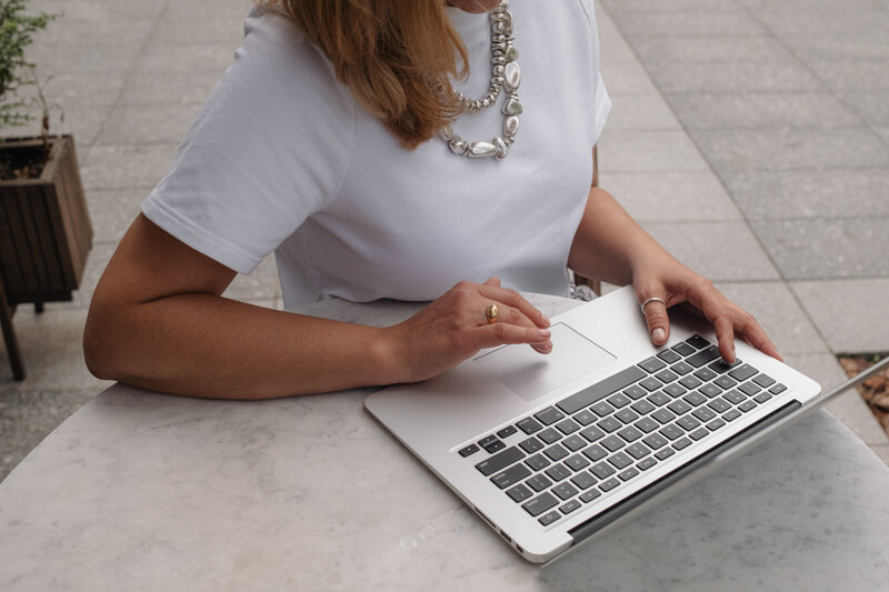 woman with a white shirt and silver necklaces on a laptop