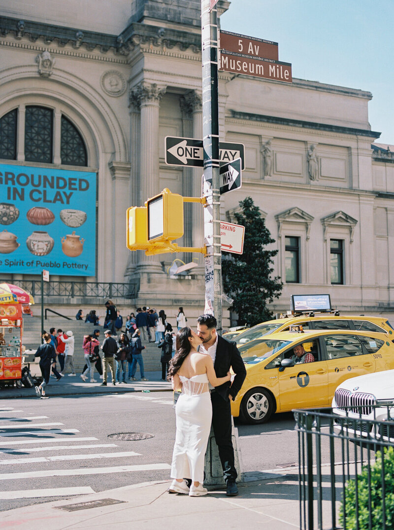 Engaged couple sharing an intimate moment in front of The Met Museum on 5th Avenue in New York City, surrounded by iconic yellow taxis and historic architecture, captured by Stephanie Michelle Photography, specializing in luxury wedding and engagement photography.