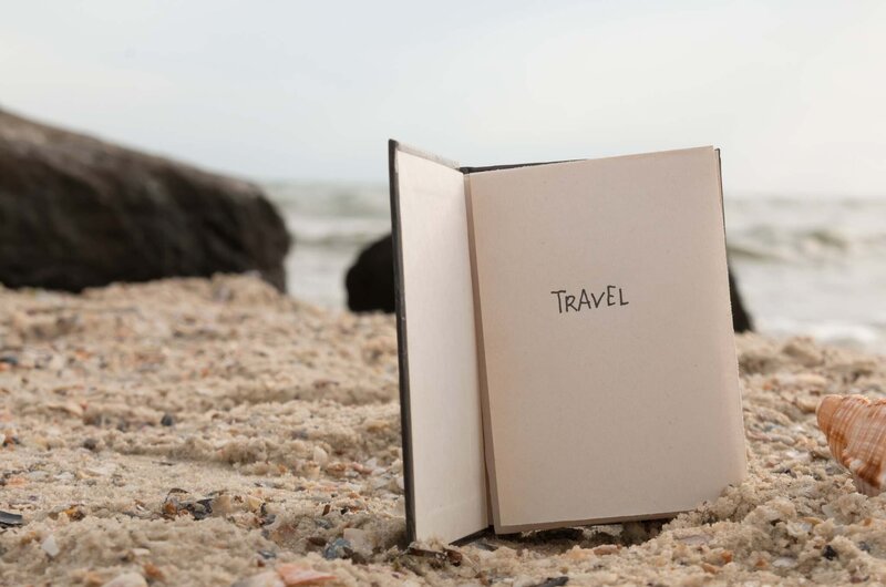 carnet avec écrit "travel" et posé sur une plage