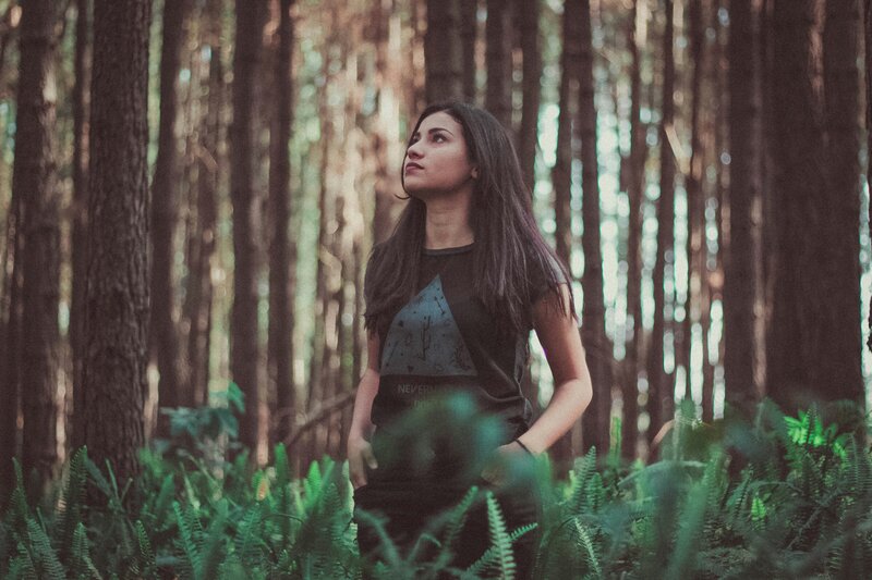 A young woman with dark hair standing in the forest looking up