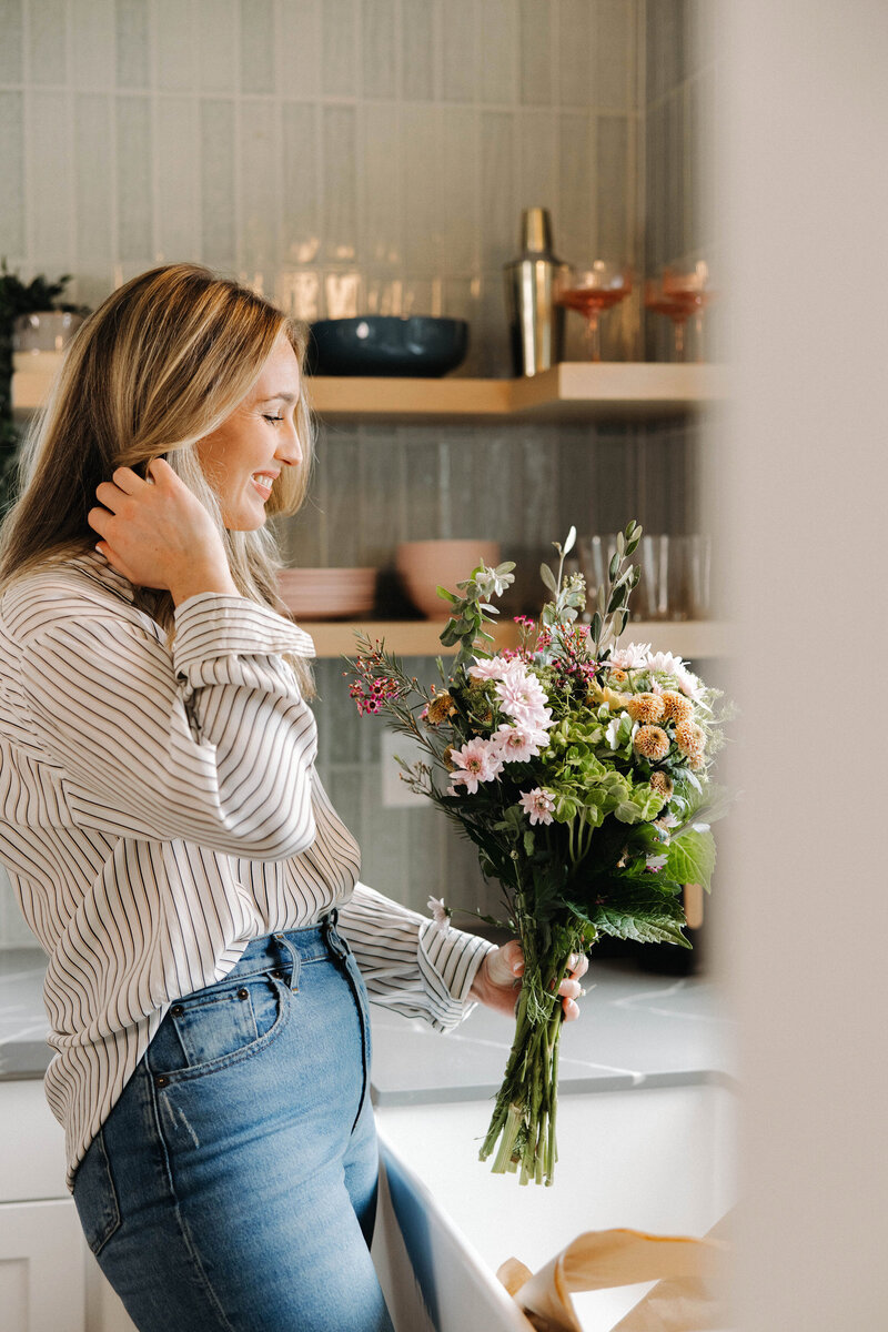 Woman in a kitchen holding flowers at the sink