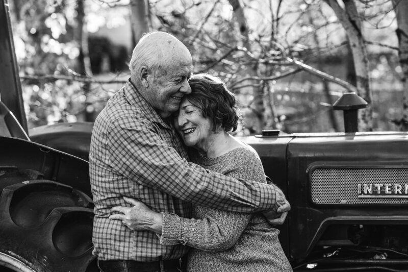 elderly couple embraces in front of vintage tractor