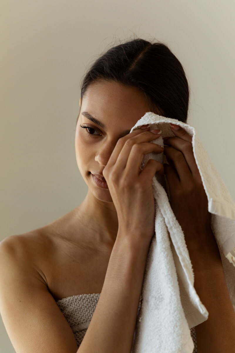 Woman gently cleansing her face with a towel during a calming skincare routine, symbolizing clean beauty, self-care, and mindful wellness practices.