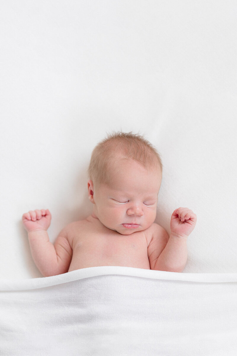 Newborn baby boy sleeping on a white backdrop covered with a white blanket