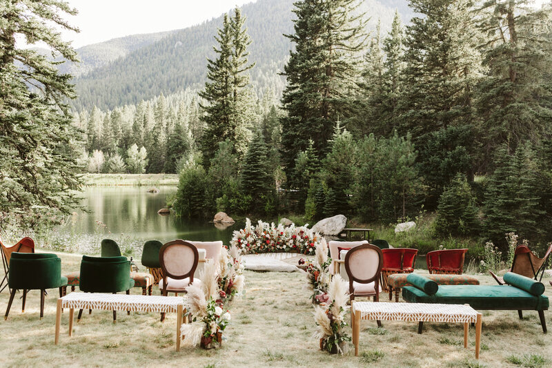 Antique chairs lined up by a lake with a mountain and trees in the background