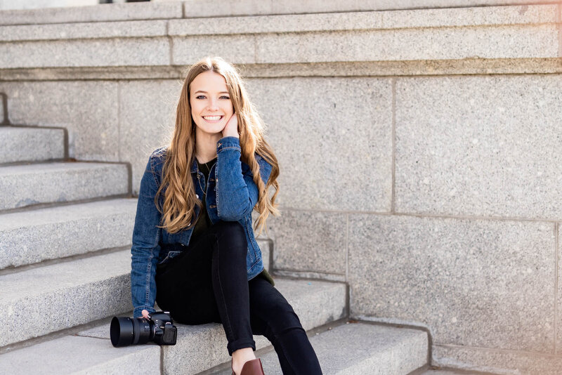 Woman holding a camera sitting on some steps and smiling