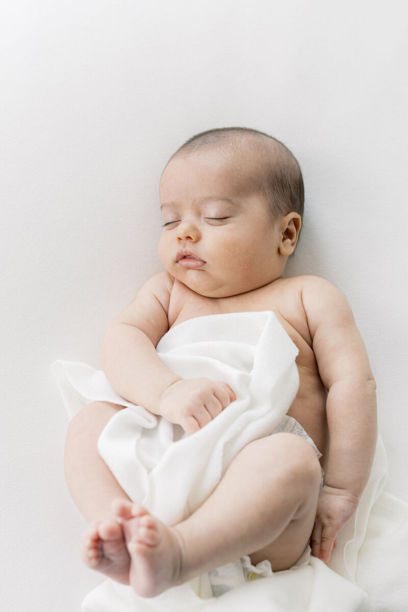 Minimal newborn portrait with baby swaddled in white on a soft cream blanket, captured in Charlotte NC studio.