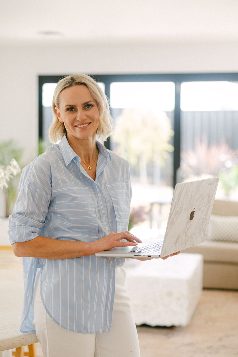 Zelda Green, financial educator, photographer and podcaster, smiling at camera holding her laptop and wearing a light blue shirt