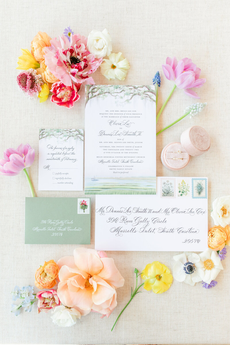 A beautifully arranged wedding invitation suite featuring delicate calligraphy, watercolor illustrations, and elegant floral accents in soft pastel tones
