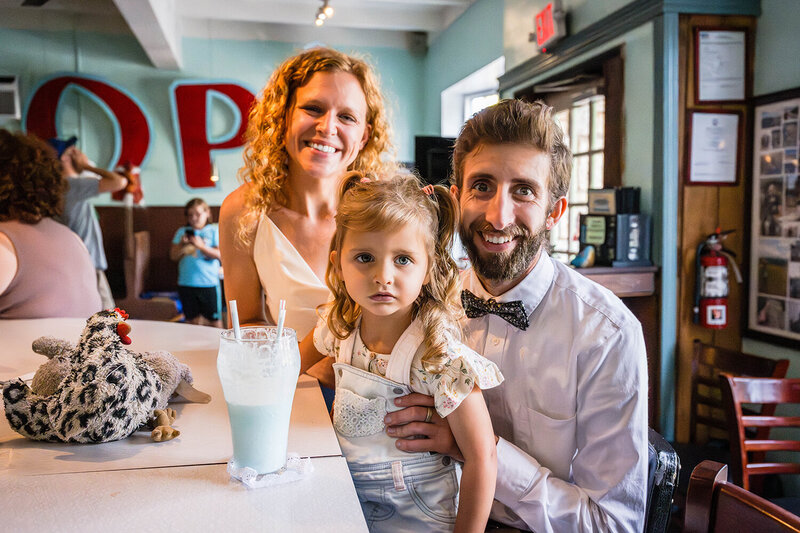 A bride, groom, and their daughter sit at the bar of Pop's Ice Cream & Soda Bar in Roanoke, Virginia and enjoy a cotton candy milkshake.