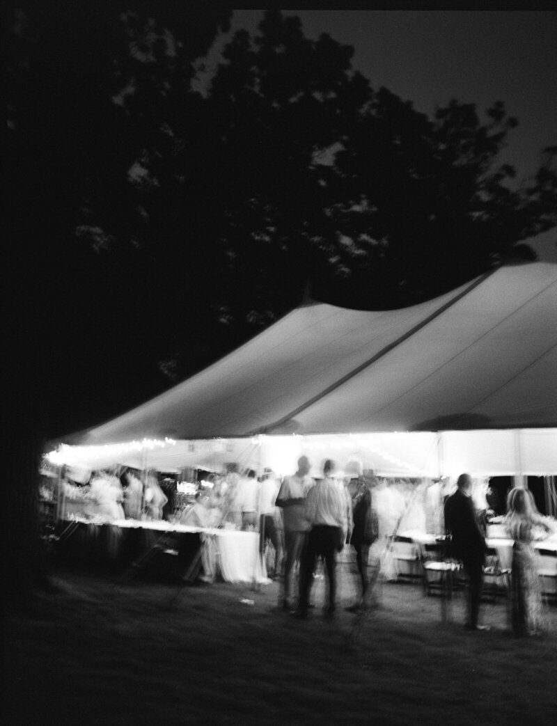 black and white night image of wedding reception guests under illuminated tent photographed by wedding photographers in minnesota tom thornton photography