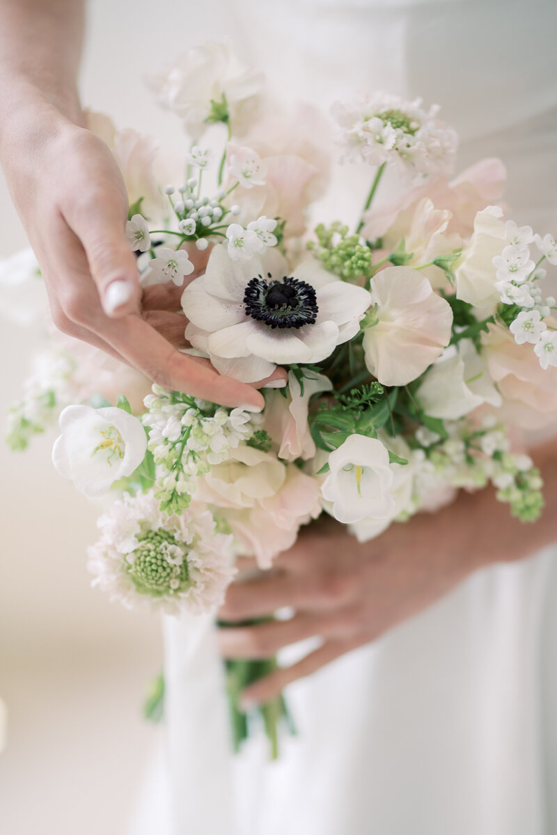 Light and airy edit of a bridal bouquet, the bride has her hand gentley placed around the flower