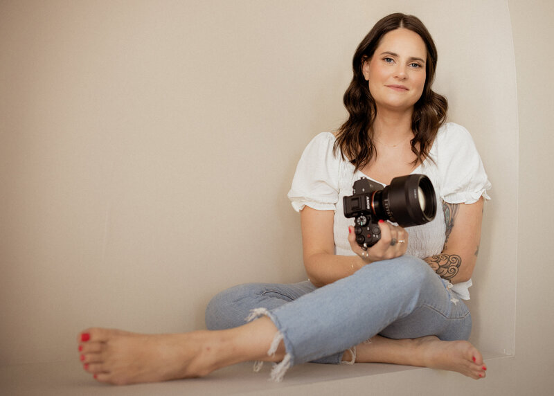 A photographer sitting on the ground with the legs crossed holding a camera 