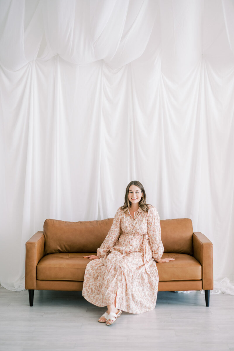 Modern calligrapher McKenna from life in letters sitting posed on a leather couch looking at camera and smiling representing full service design and calligraphy by Life in Letters.