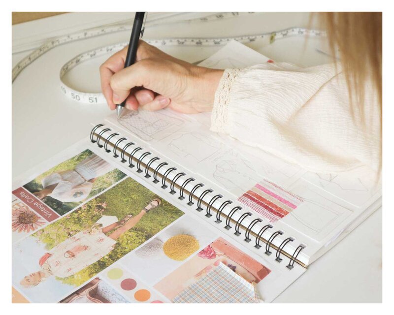 Doreen Apparel designer sketching women's fashion ideas in a notebook with color palettes and fabric swatches for collection planning