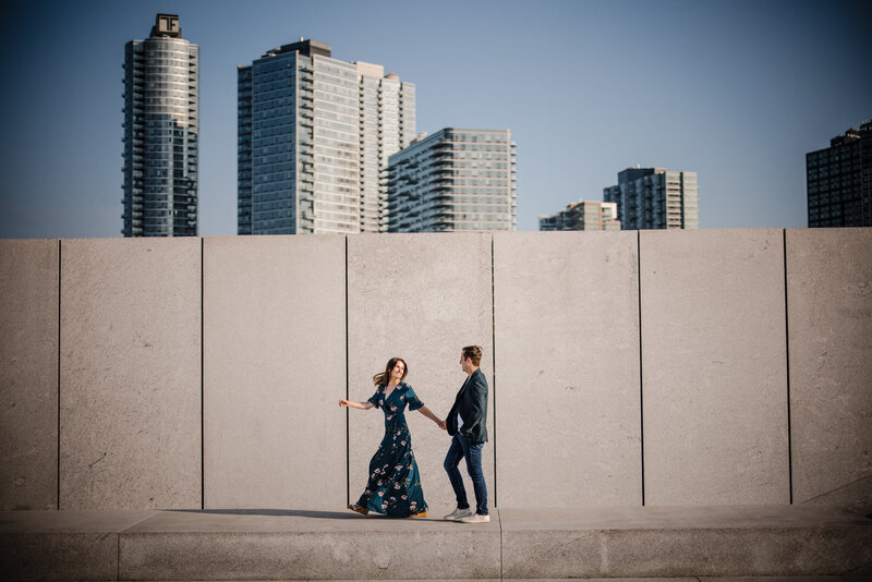 A couple walking along a sidewalk together with skyscrapers behind them.