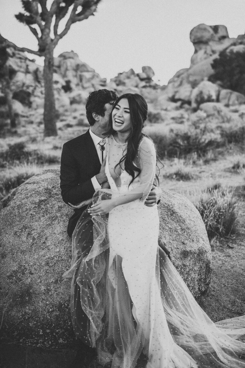 Joshua Tree elopement with couple leaning against rock snuggling and laughing