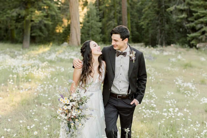 A bride and groom enjoy a walk in mountain meadow of wildflowers on their wedding day. 