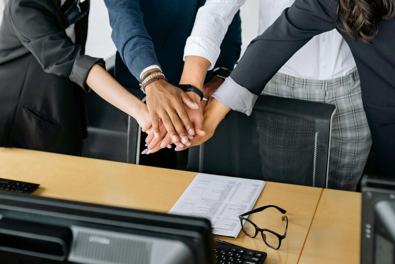 A close-up image showing a diverse group of hands stacked together over a desk, symbolizing teamwork and unity.